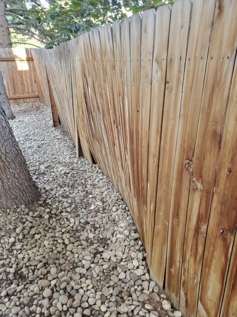 image of warped fence due to weight of river rock at its base