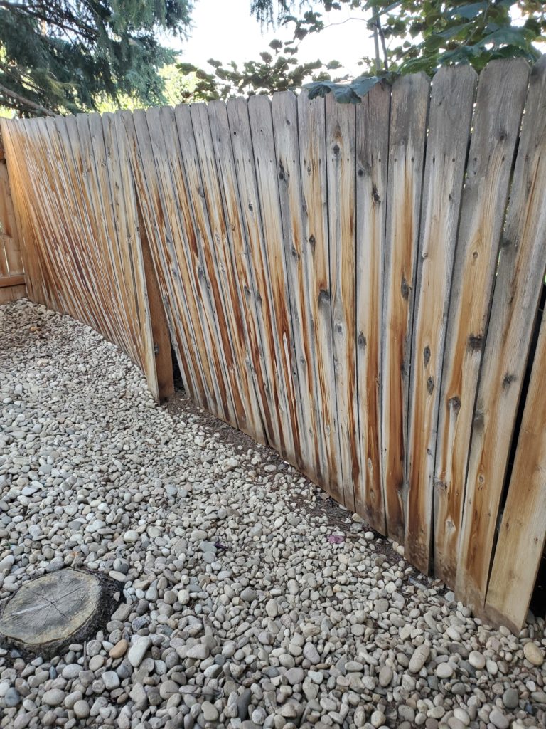 Image of warped fence due to weight of river rock at its base